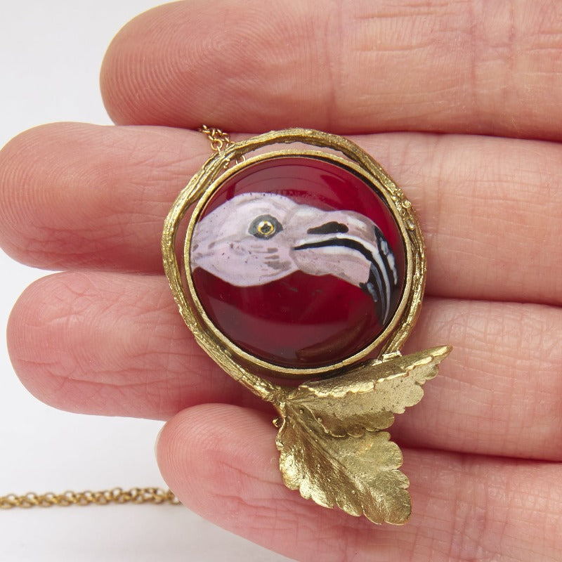 Hand-painted pink flamingo head on upcycled glass cabochon, set in an 18k gold-plated, handmade botanical round setting. Delicate miniature painting setted in a round frame featuring a realistic small tree branch with two small leaves.