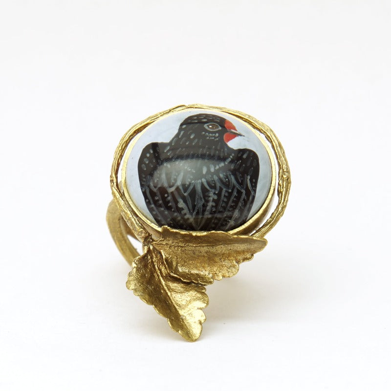 Hand-painted swallow on upcycled glass cabochon, set in an 18k gold-plated, handmade botanical round setting statement ring. Delicate miniature painting setted in a round setting featuring a realistic small tree branch with two small leaves. Light blue background. Realistic adjustable tree branch ring.