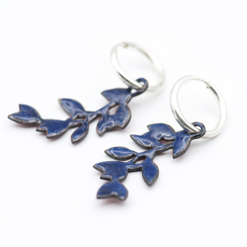 Sterling silver hoop earrings featuring a stylized dangling leafy branch crafted with glass enamel cloisonné on copper. Back of the leaf branch in dark blue counter-enamel