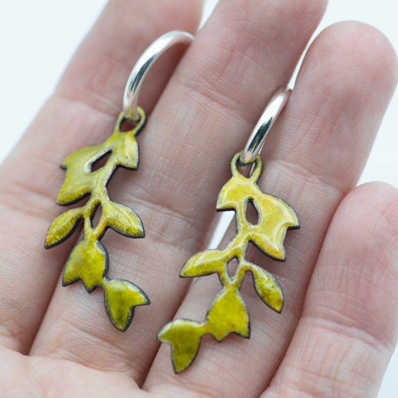 Sterling silver hoop earrings featuring a stylized dangling leafy branch crafted with glass enamel cloisonné on copper. Yellow colour enamel