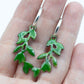 Sterling silver hoop earrings featuring a stylized dangling leafy branch crafted with glass enamel cloisonné on copper. Green colour enamel