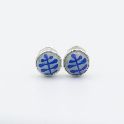 Medium round cabochon studs in sterling silver and glass, featuring a delicate painting of a stylized round leaf. Grey background and blue leaf.