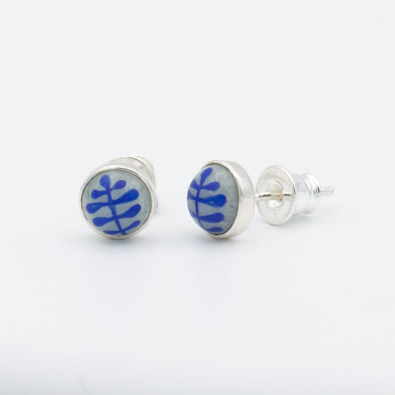 Medium round cabochon studs in sterling silver and glass, featuring a delicate painting of a stylized round leaf. Grey background and blue leaf.