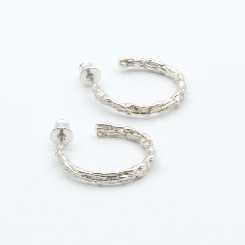 Medium round sterling silver hoop earrings with an organic texture reminiscent of sand dripping at the beach. Smooth surface with tactile appeal and visually captivating design. Sterling silver