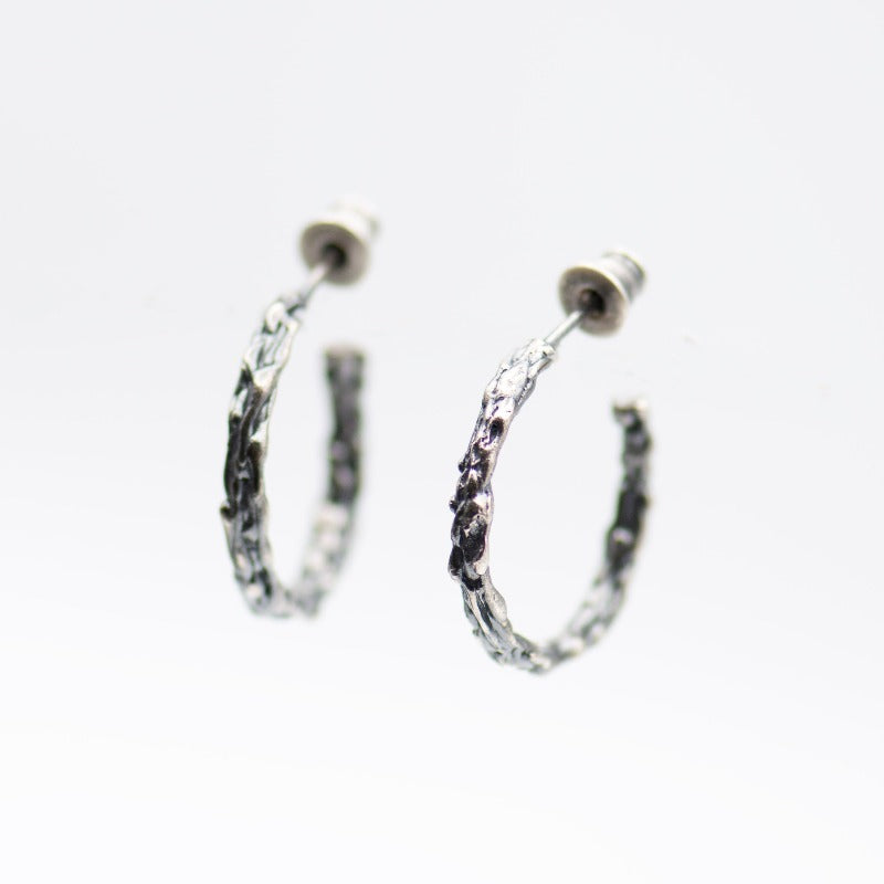 Medium round sterling silver hoop earrings with an organic texture reminiscent of sand dripping at the beach. Smooth surface with tactile appeal and visually captivating design. Black oxidized sterling silver