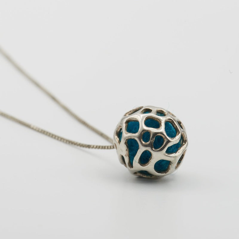 Sterling silver pendant featuring a simple hollow organic shape with colored wool inside, visible through the outer layer. The sphere measures approximately 1.5 cm, paired with a 60 cm sterling silver chain. Blue wool 